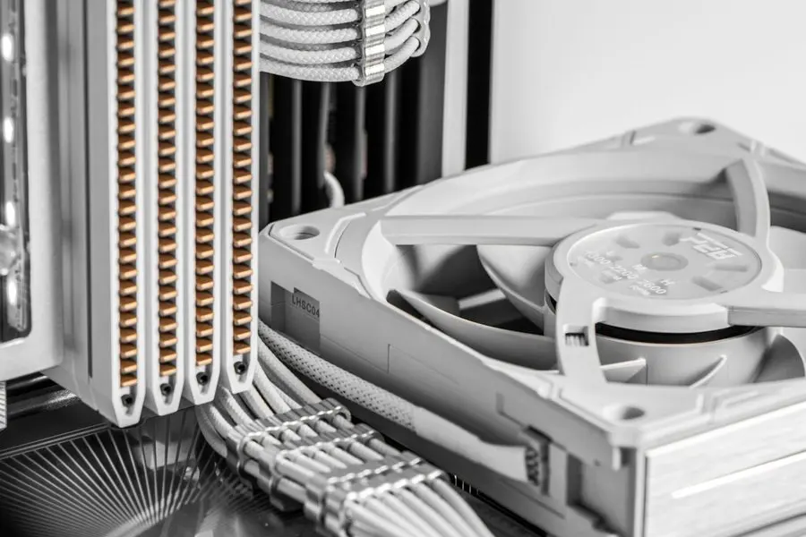 Close-up inside a light grey desktop computer case showing a large white square cooling fan with its hub and blades, a tall heatsink with rows of copper heat pipes, white braided cables, and a vented case panel.
