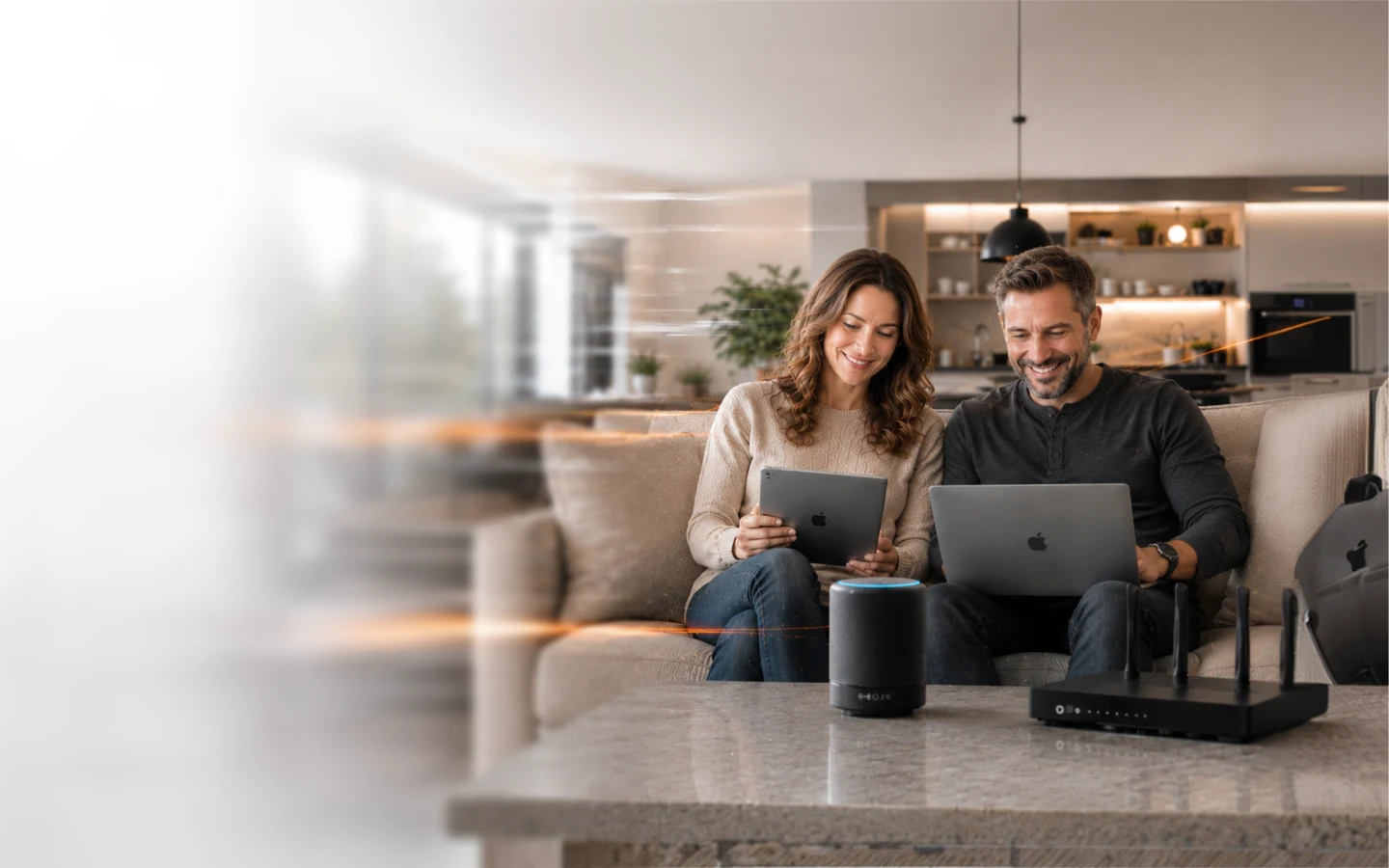A couple on their living-room sofa sharing a laptop and tablet, with a WiFi router and smart speaker on the table beside them
