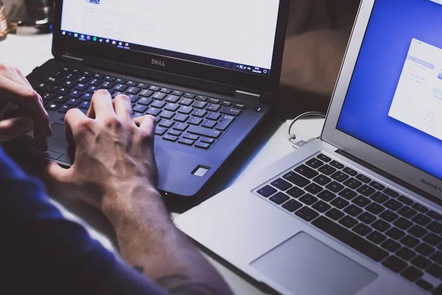 Hands working on a laptop keyboard beside a second screen