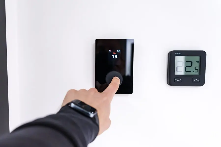 A finger adjusting a wall-mounted smart thermostat