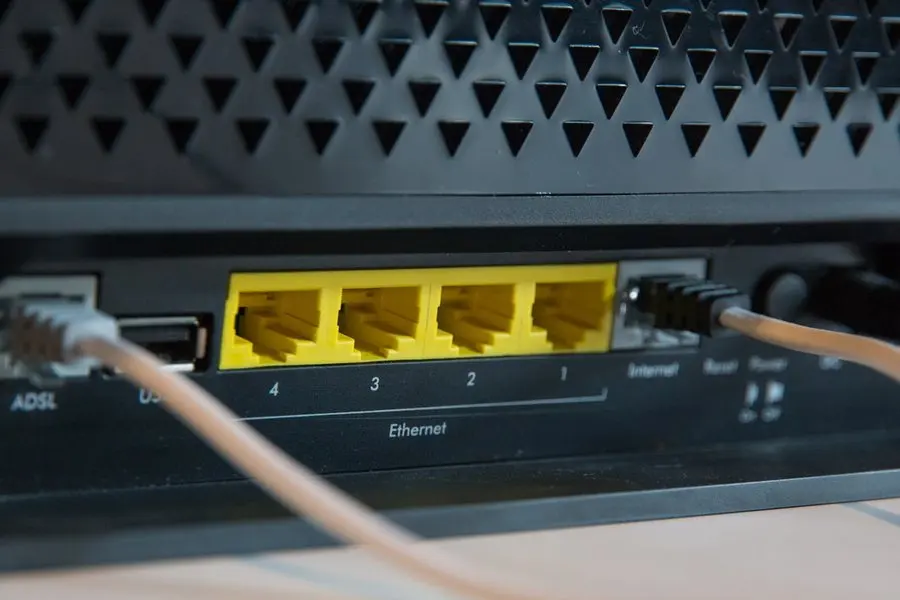 Close-up of the back of a black router: a bank of four yellow ethernet ports labelled 1 to 4, with pale network cables plugged into the ADSL and internet sockets beside them.